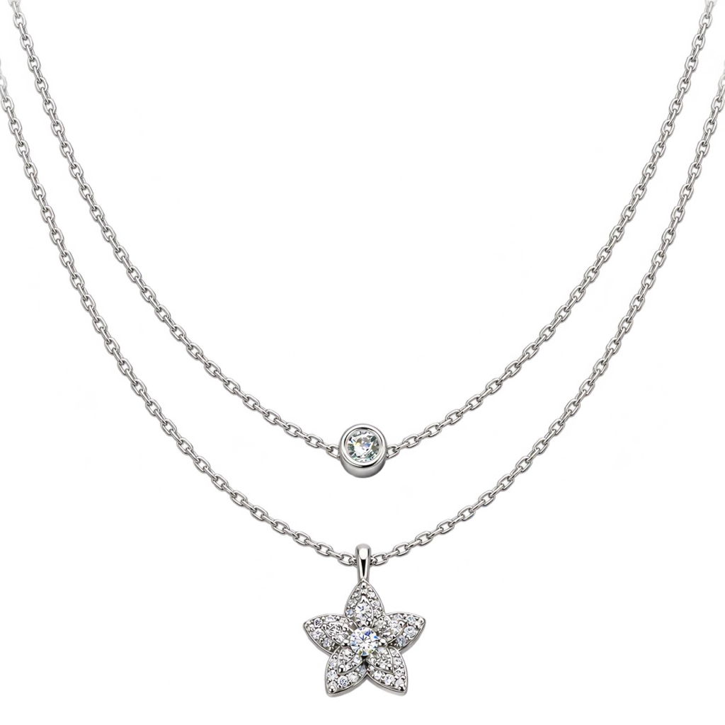 Double-layer silver necklace resting against a white background, featuring a shorter chain with a single bezel-set cubic zirconia and a longer chain suspending a stone-encrusted star flower pendant